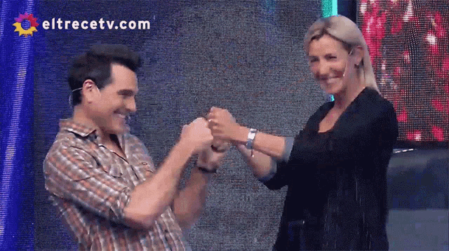 a man and a woman are shaking hands in front of a screen that says eltrecetv.com