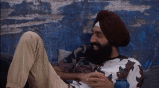 a man with a beard wearing a turban is sitting on a couch with his legs crossed .