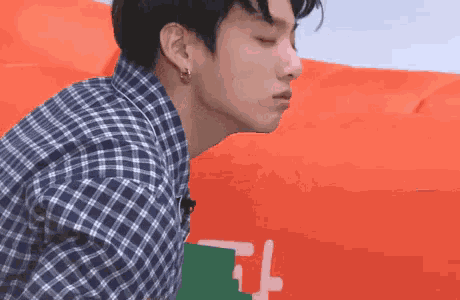 a young man wearing a plaid shirt and earrings is standing in front of a red inflatable balloon .