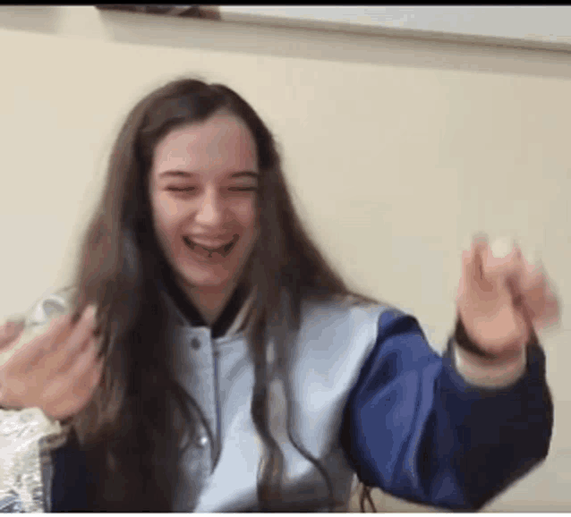 a girl with long hair wearing a blue and white jacket is laughing .