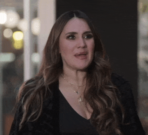 a woman with long hair is wearing a black jacket and necklace .