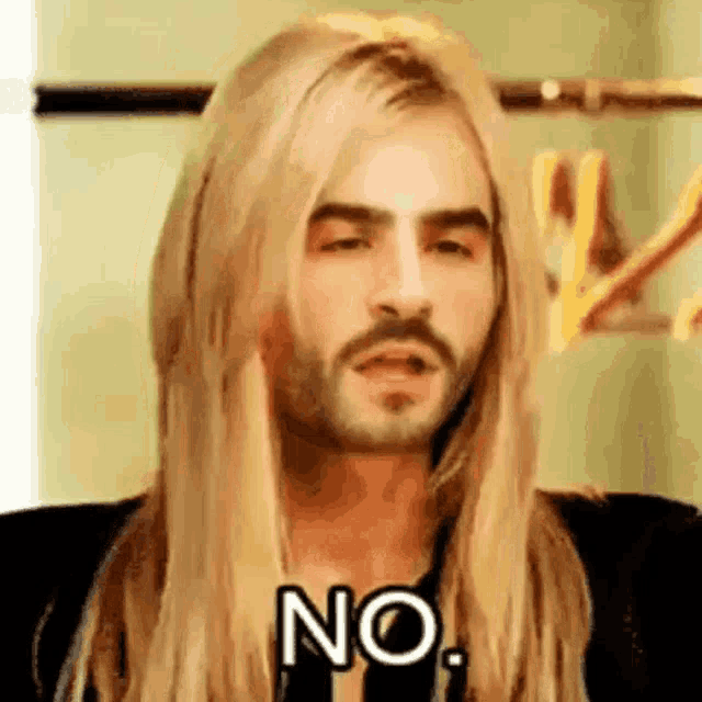 a man with long blonde hair and a beard is holding his hand to his face and saying no .