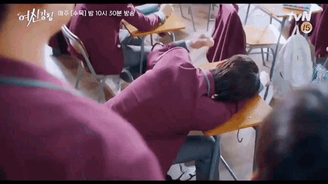 a girl is laying on a desk in a classroom while a group of people sit at desks .