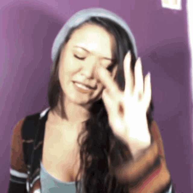 a woman wearing a beanie and a sweater is making an ok sign with her hand .