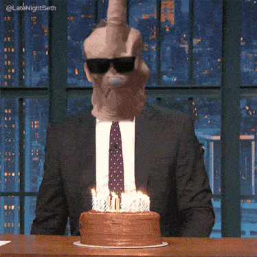 a man in a suit and tie is blowing out candles on a cake