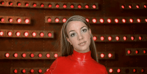 a woman in a red turtleneck is standing in front of a wall of red lights