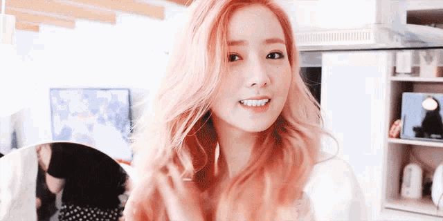 a woman with long pink hair is smiling and looking at the camera