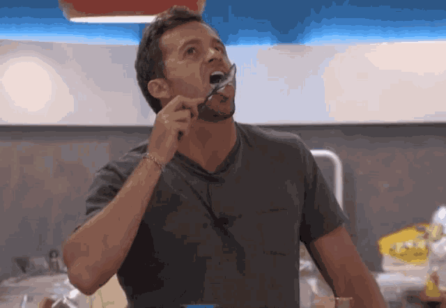 a man in a gray shirt is brushing his teeth with a toothbrush