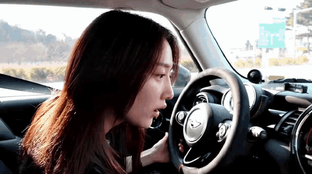 a woman is driving a car with a green sign in the background that says ' exit 1 '