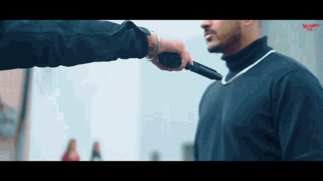 a man in a black turtleneck is being threatened by another man with a gun