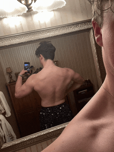a shirtless man taking a picture of his back in a mirror