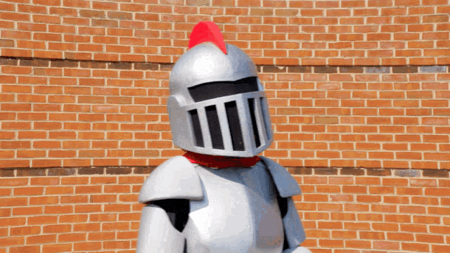 a mascot in a knight 's armor salutes in front of a brick wall