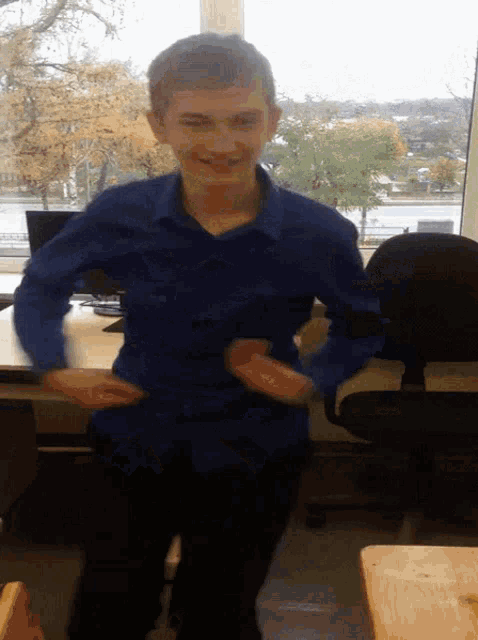 a young man in a blue shirt is standing in front of a window