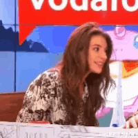 a woman is sitting in front of a red sign that says vodafone