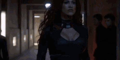 a woman with red hair is standing in a dark hallway with a man in the background .
