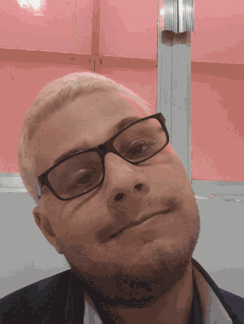 a man wearing glasses and a beard is smiling in front of a pink wall
