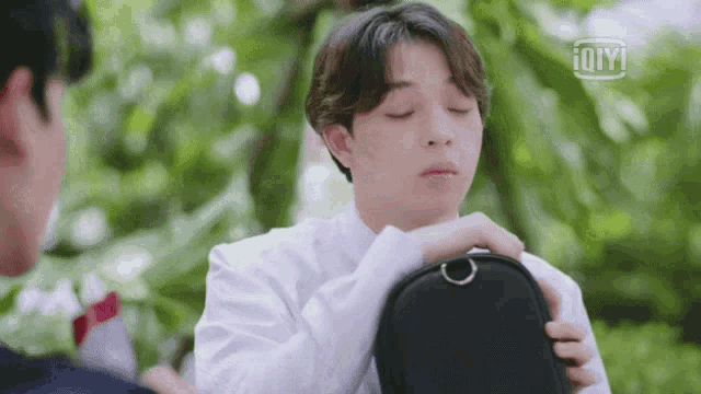 a young man in a white shirt is holding a black purse .