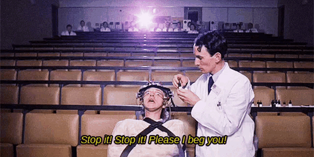 a man in a lab coat is talking to a man in a straitjacket in an auditorium