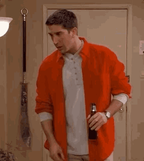 a man wearing a red shirt is holding a bottle of beer .