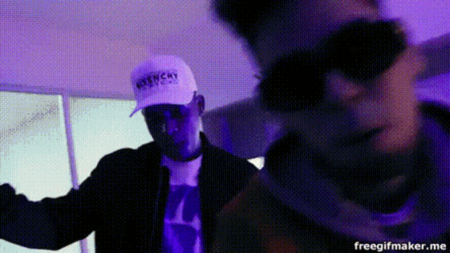 a man wearing a hat and sunglasses is dancing in a room with purple lights .