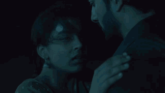 a man with a bandage on his head is kissing a woman in a dark room .