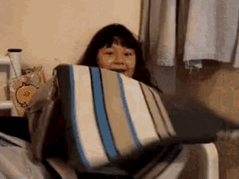 a girl is sitting in a chair with a striped pillow in her mouth .
