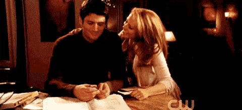 a man and a woman are sitting at a table with a cw logo in the background .