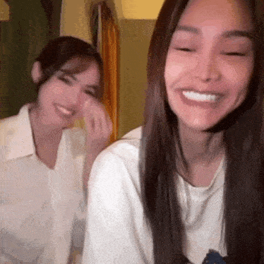 two women are smiling and laughing together while sitting next to each other in a room .