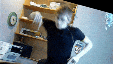 a man in a black shirt is standing in front of a shelf with a clock on it