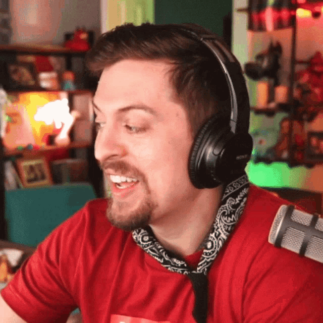 a man wearing headphones and a red shirt with a bandana around his neck is smiling