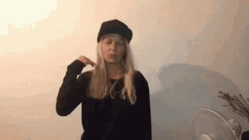 a young woman wearing a black hat and a black shirt is standing in front of a fan .