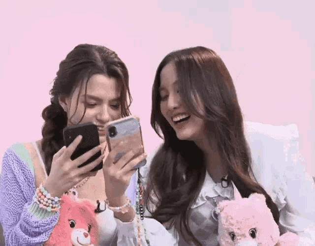 two women are sitting next to each other and looking at their phones .