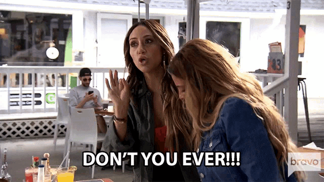 two women are sitting at a table and one of them is saying " don 't you ever !!! "