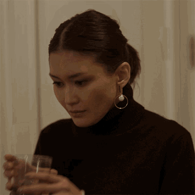 a woman in a black turtleneck is holding a glass