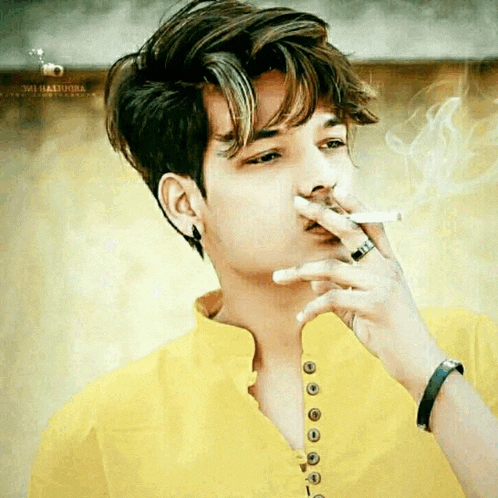 a young man in a yellow shirt is smoking a cigarette with a ring on his finger