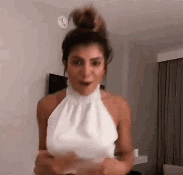 a woman in a white halter top is standing in a room with her hair in a bun .