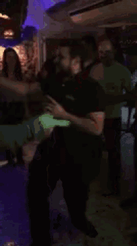 a man in a black shirt is dancing in a dark room with purple lights