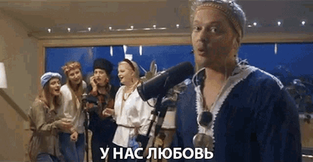 a man is singing into a microphone while a group of women are standing behind him .