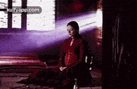 a woman in a red dress is sitting on the floor in a dark room .