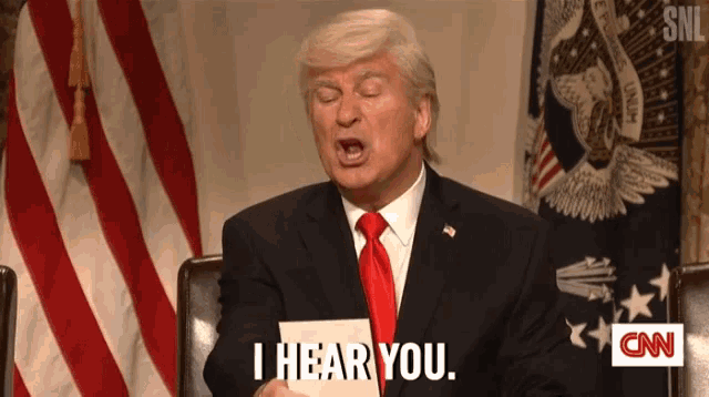 a man in a suit and tie is standing in front of an american flag and says i hear you .