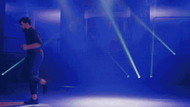 a man in a black shirt is dancing on a stage with purple lights behind him