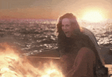 a woman is sitting on a boat near a fire in the ocean