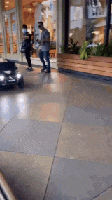 a man in a gray shirt is walking down a sidewalk next to a woman in a mask .