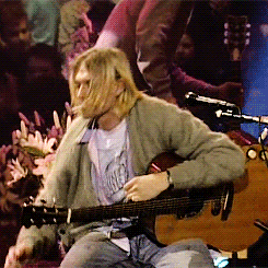 a man playing a guitar with a t-shirt that says ' nirvana ' on it