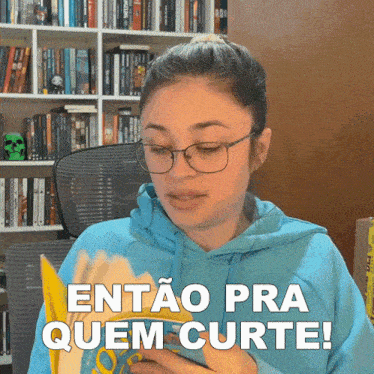 a woman wearing glasses and a blue hoodie holds a book and says entao pra quem curte