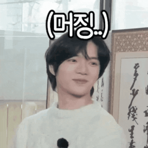 a young man in a white sweater is standing in front of a framed picture with chinese writing on it .