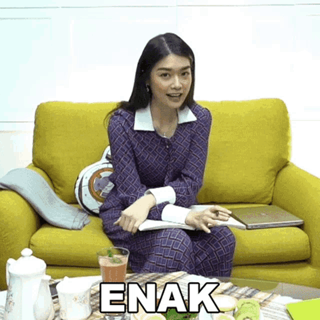 a woman sits on a yellow couch next to a table with the word enak written on it
