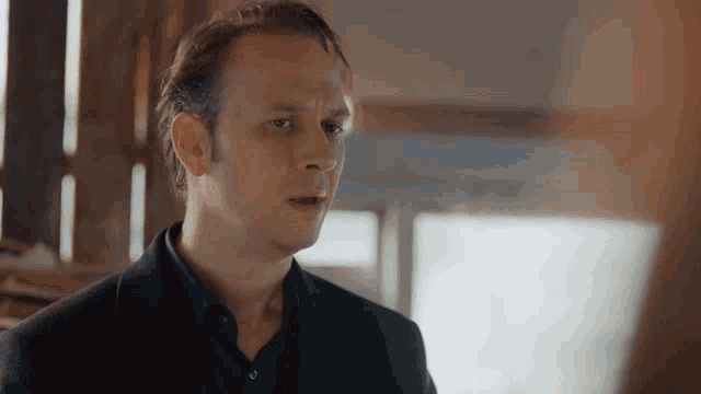 a man in a black suit and black shirt looks to his left