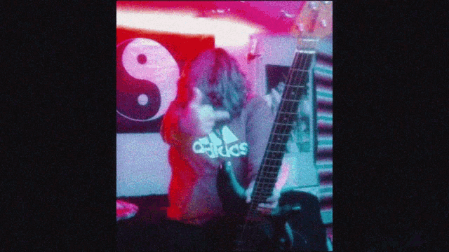 a woman playing a guitar with an adidas shirt on