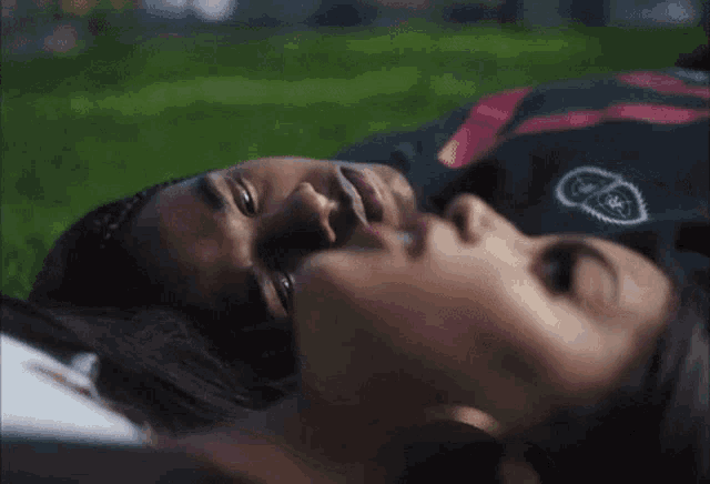 a man and a woman are laying on the grass and the man is wearing a shirt with the letter s on it